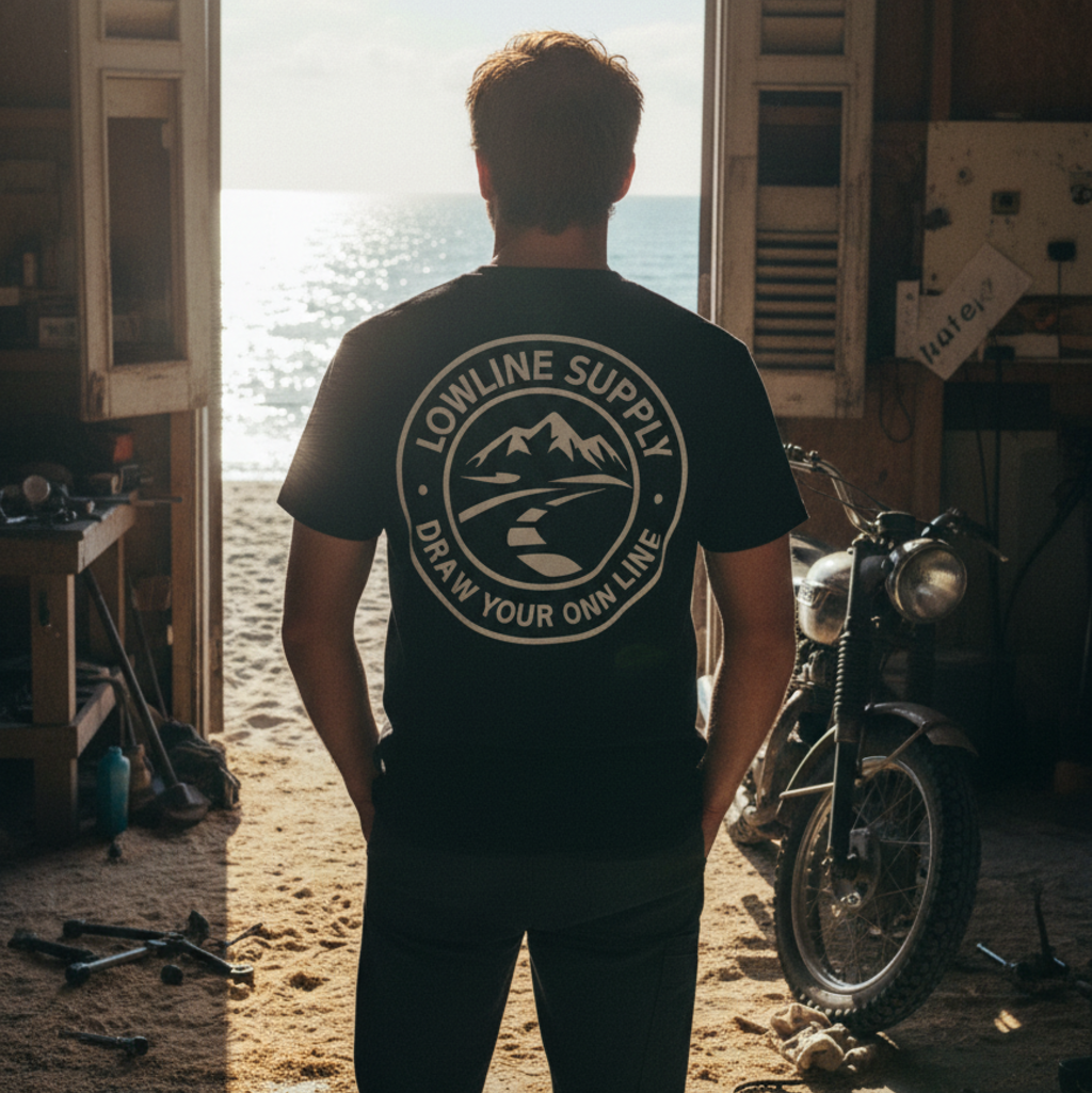 Person wearing a black t-shirt with 'Lowline Supply' logo standing in a garage with an open door leading to a beach.